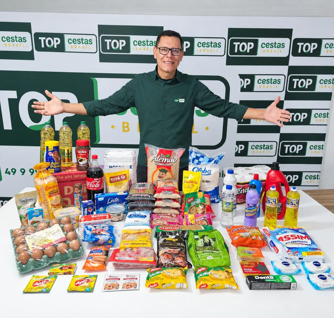 Aparício, da Top Cestas Brasil, de braços abertos atrás da mesa com os itens do Kit Família